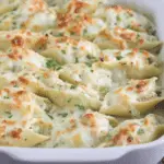 A white baking dish filled with golden, cheesy Chicken Alfredo Stuffed Shells garnished with chopped parsley.