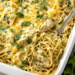 A baking dish filled with creamy chicken tetrazzini, topped with melted cheese and chopped parsley, with a serving spoon inside.