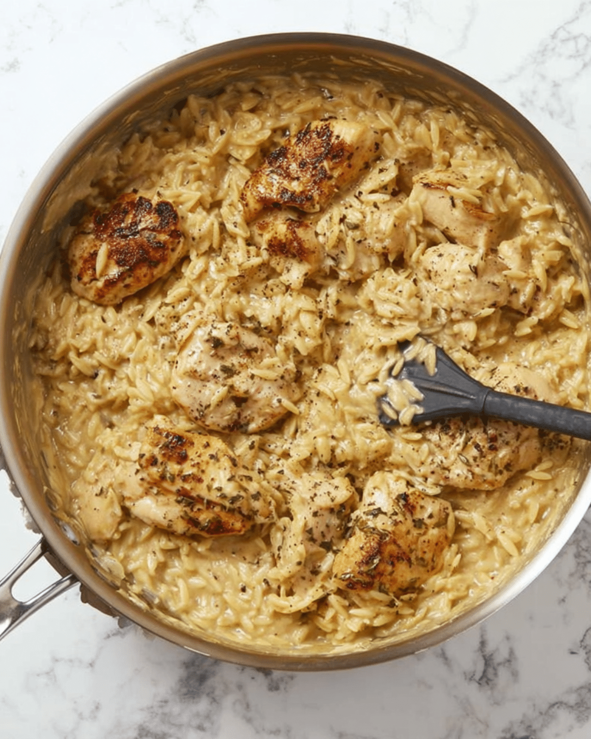 Creamy Chicken and Orzo Skillet with seared chicken pieces and seasoned orzo in a stainless steel pan.