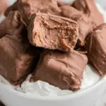 A bowl filled with chocolate-covered Cool Whip candy pieces, with one piece bitten to reveal a creamy interior.