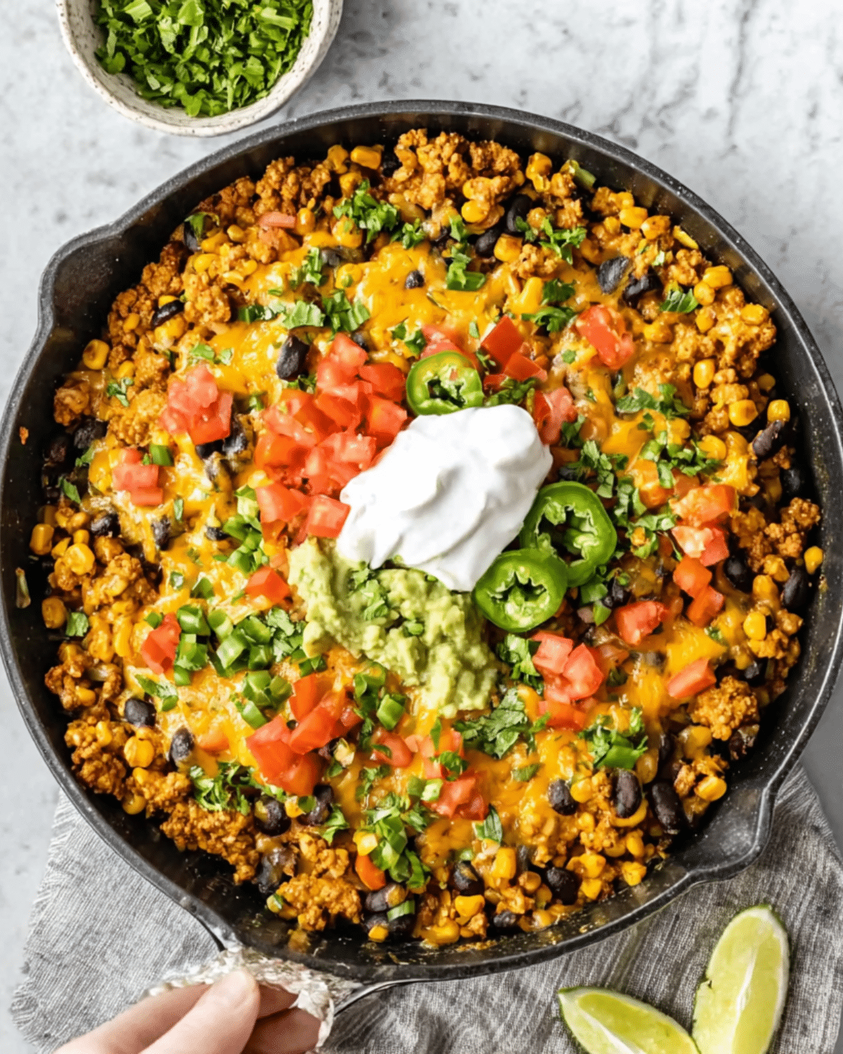 Ground turkey taco skillet filled with corn, black beans, melted cheese, tomatoes, jalapeños, guacamole, and sour cream in a black cast iron pan.