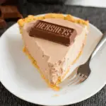 Slice of creamy Hershey Pie topped with a piece of Hershey's chocolate bar on a white plate.