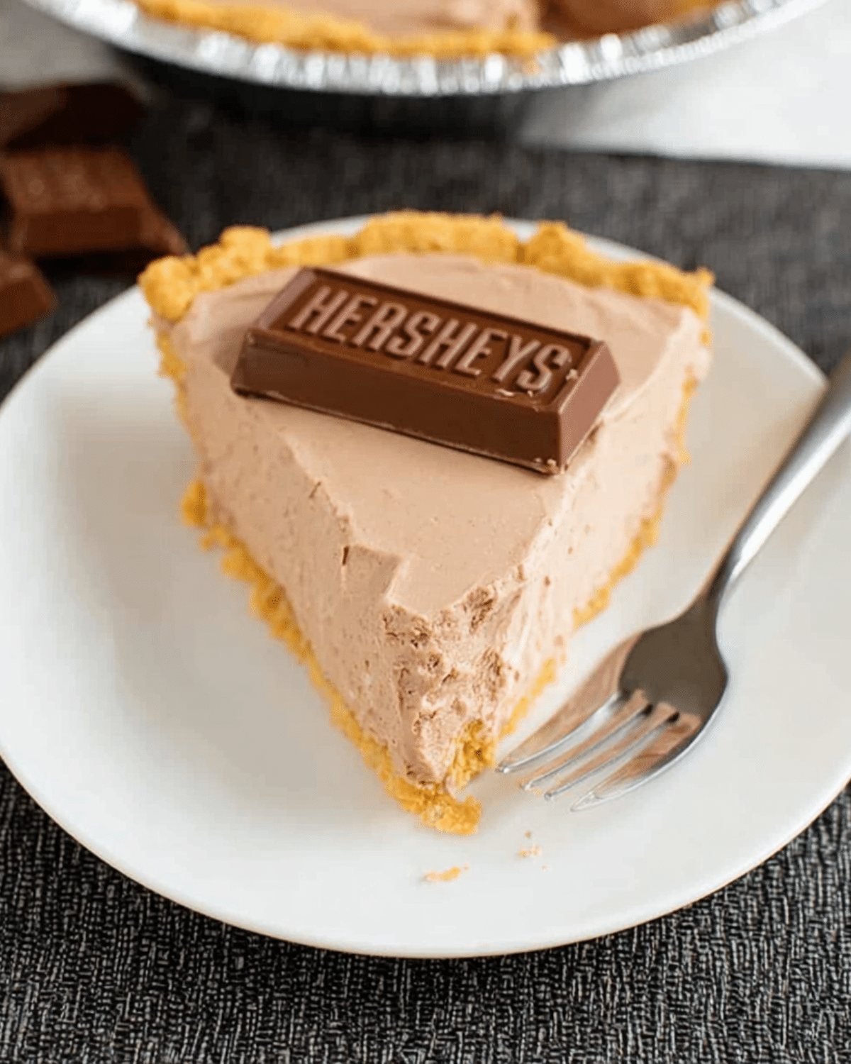 Slice of creamy Hershey Pie topped with a piece of Hershey's chocolate bar on a white plate.