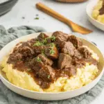 Plate of Slow Cooker Beef Tips served over creamy mashed potatoes, topped with rich brown gravy and garnished with chopped parsley.