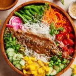 Spring Roll Salad with Peanut Dressing in a wooden bowl, topped with fresh vegetables, rice noodles, and sesame seeds.