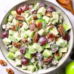 Bowl of Waldorf Salad filled with green apples, red grapes, celery, pecans, and fresh herbs coated in a creamy dressing.