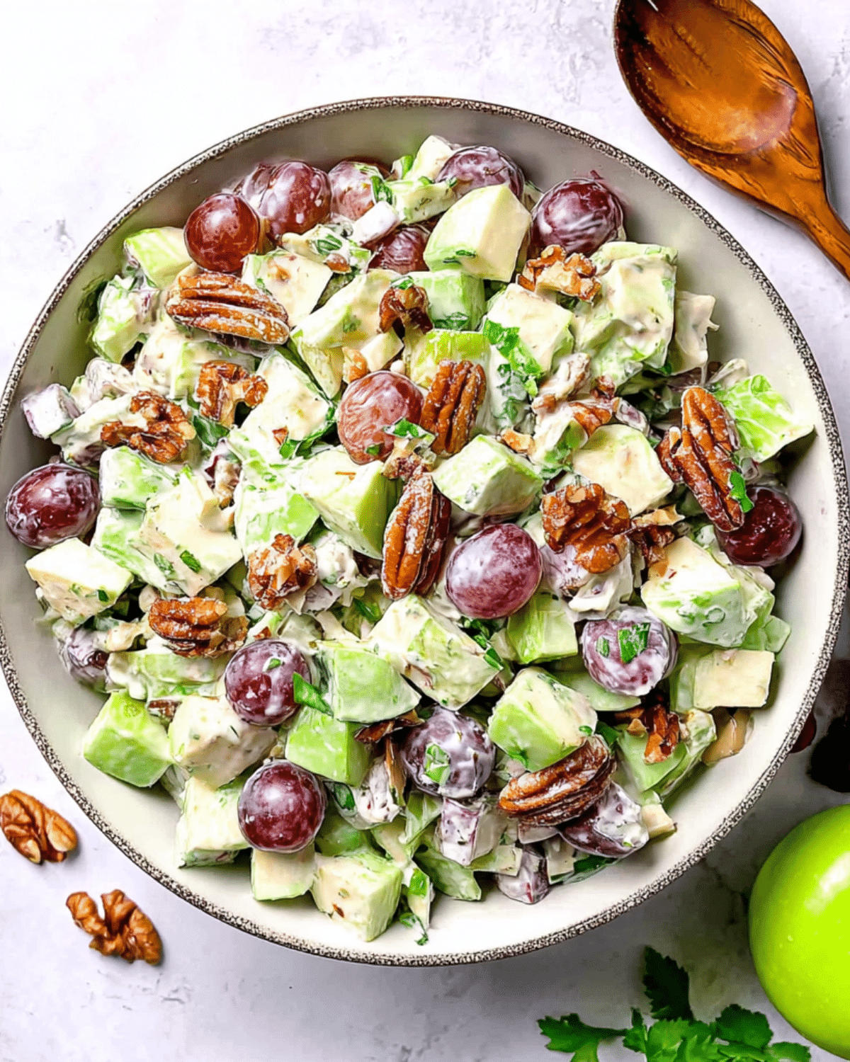 Bowl of Waldorf Salad filled with green apples, red grapes, celery, pecans, and fresh herbs coated in a creamy dressing.
