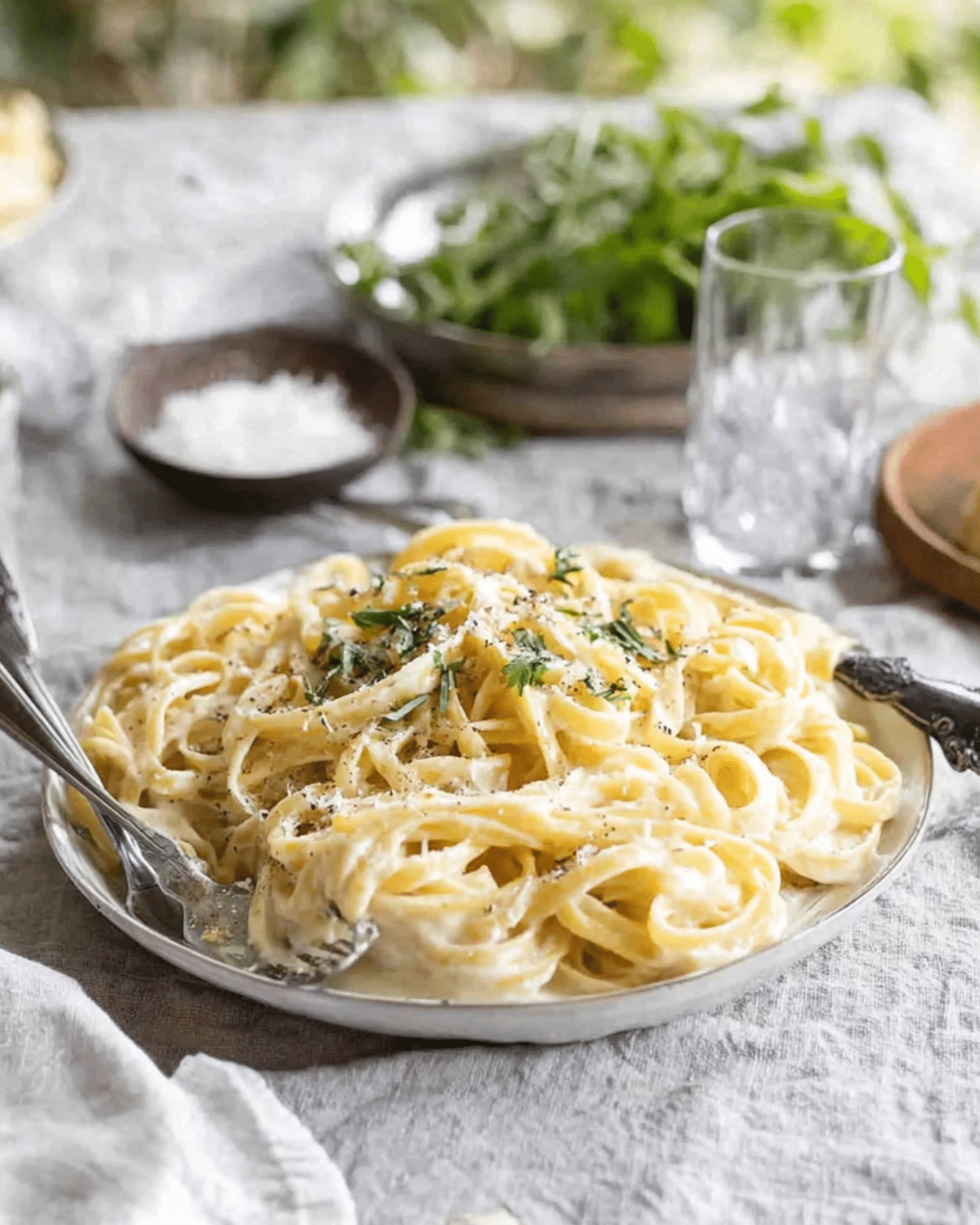 Plate of creamy fettuccine alfredo garnished with fresh herbs and cracked black pepper, served on a rustic table setting.
