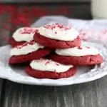 Plate of red velvet sugar cookies topped with cream cheese frosting and red sprinkles.