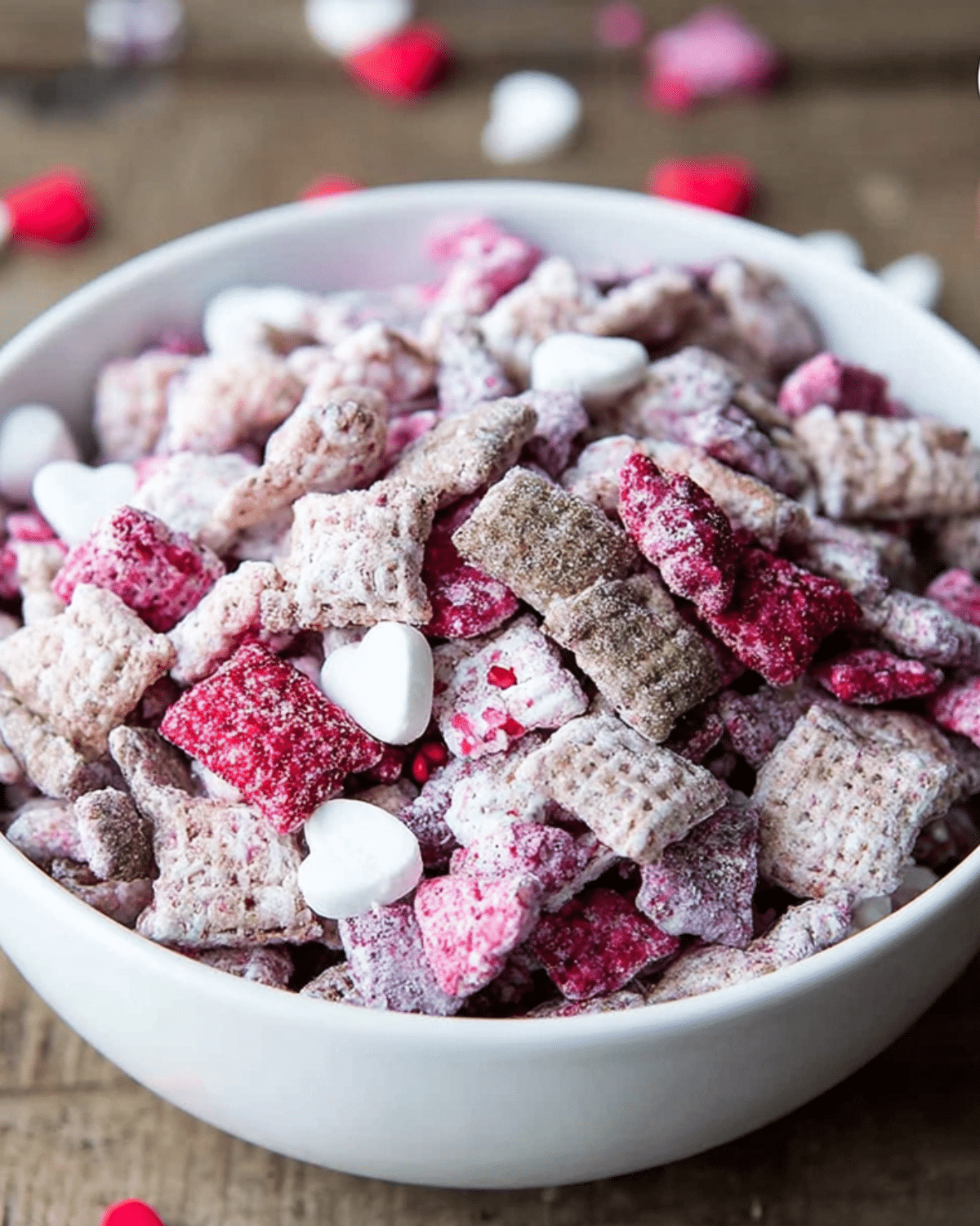 Bowl of colorful Valentine puppy chow with pink, red, and white coated cereal and heart-shaped candies.
